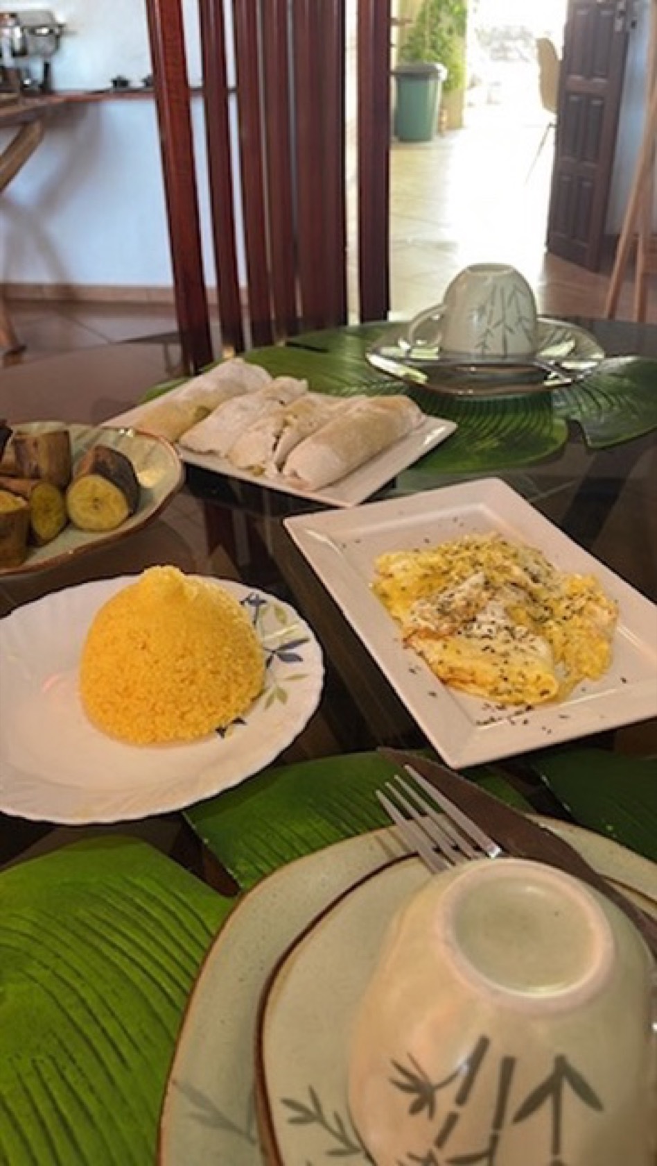 Cuscuz, omelete e frutas servidos sobre folhas de bananeira, com a vista ao fundo